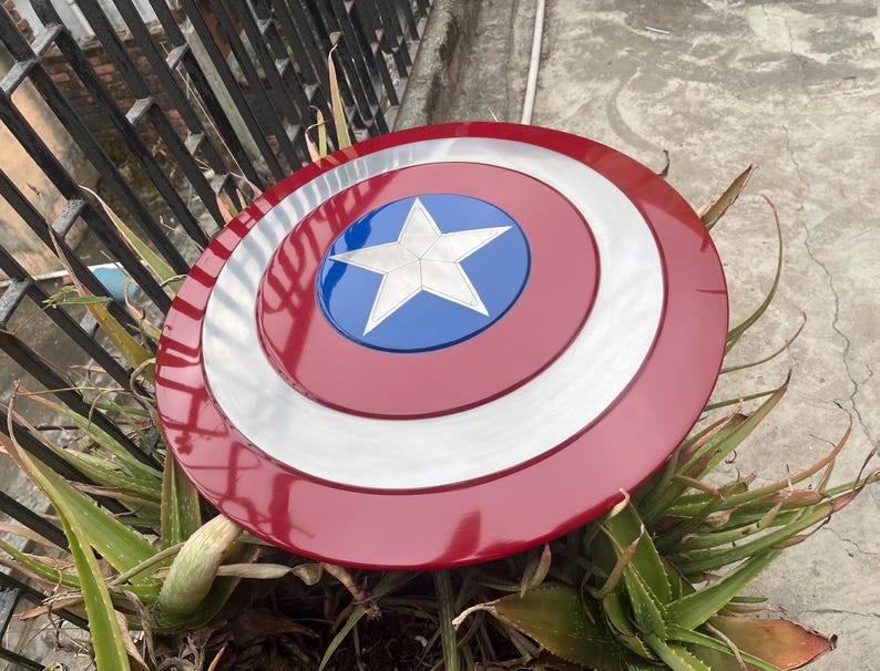 May include: A red, white, and blue Captain America shield with a five-pointed star in the center. The shield is made of metal and has a shiny finish.