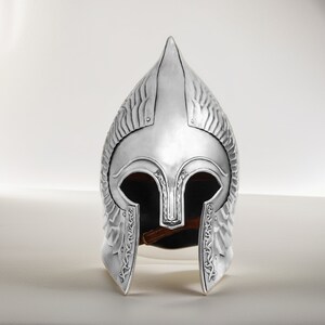 May include: A silver helmet with a pointed top and intricate details. The helmet has a face mask with eye holes and a decorative design.