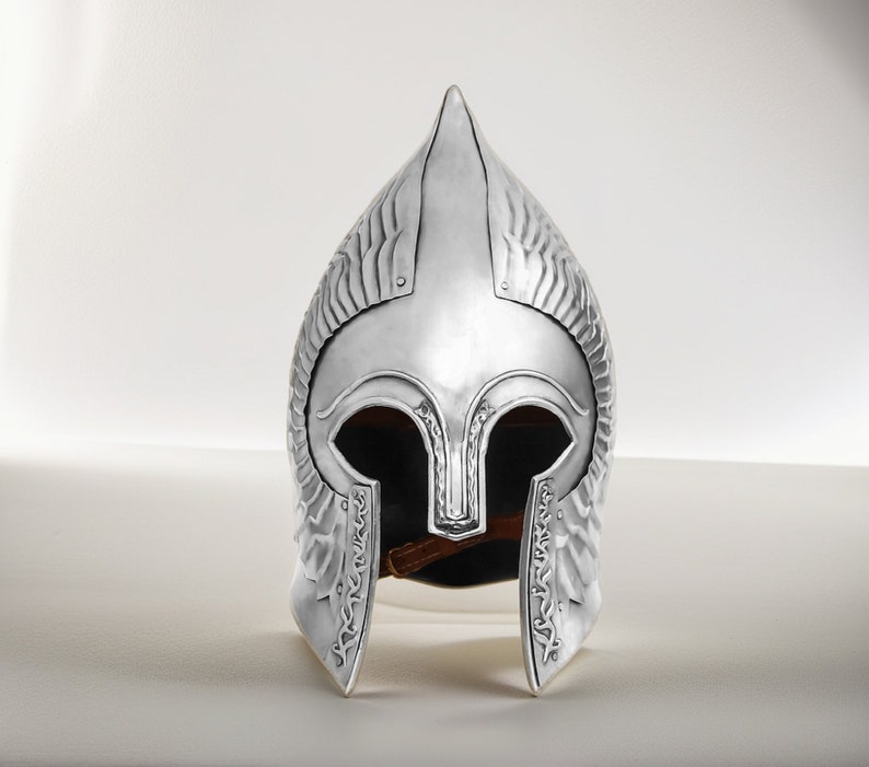 May include: A silver helmet with a pointed top and intricate details. The helmet has a face mask with eye holes and a decorative design.
