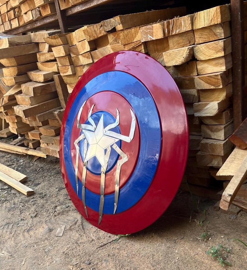 Puede incluir: Un escudo de Capit&aacute;n Am&eacute;rica rojo, blanco y azul con un dise&ntilde;o de ara&ntilde;a plateado en el centro.