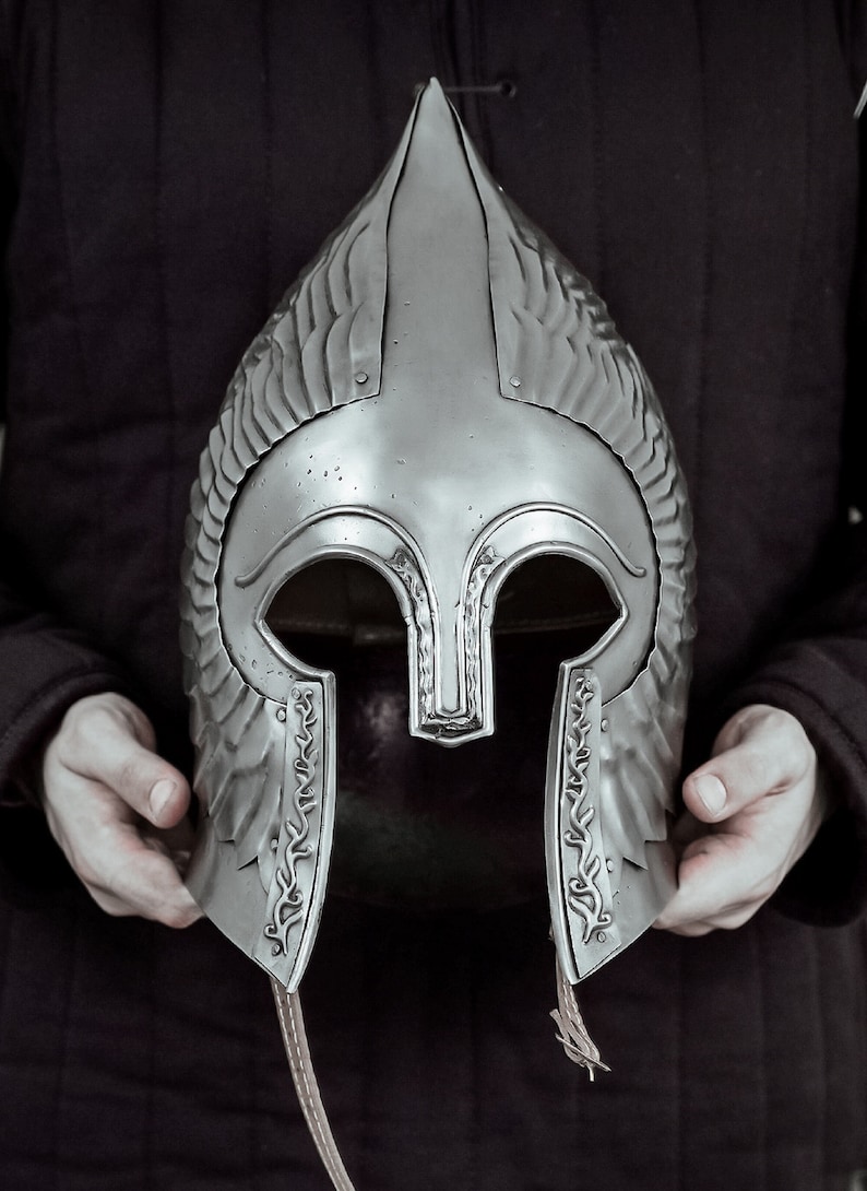 May include: A silver helmet with a pointed top and decorative details. The helmet has a face mask with eye holes and a chin strap.