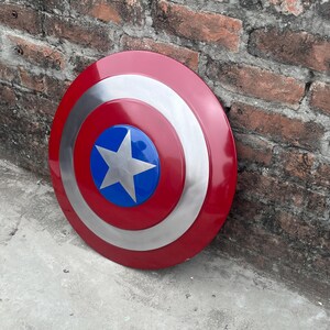 May include: A red, white, and blue Captain America shield with a silver star in the center. The shield is leaning against a brick wall.