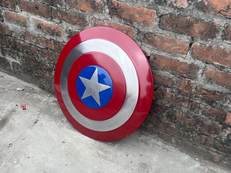 May include: A red, white, and blue Captain America shield with a silver star in the center. The shield is leaning against a brick wall.