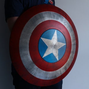 May include: A red, white, and blue Captain America shield with a silver star in the center. The shield is slightly weathered and has a distressed look.