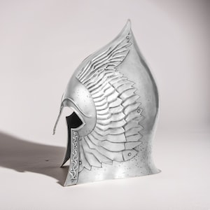 May include: A silver helmet with a winged design. The helmet is made of metal and has a textured surface.