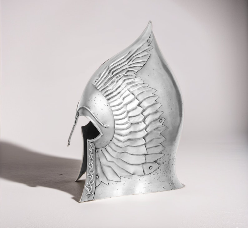 May include: A silver helmet with a winged design. The helmet is made of metal and has a textured surface.