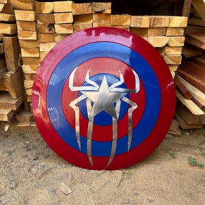 Puede incluir: Un escudo redondo rojo, blanco y azul con una estrella plateada y un dise&ntilde;o de ara&ntilde;a. El escudo es redondo y tiene un borde elevado.