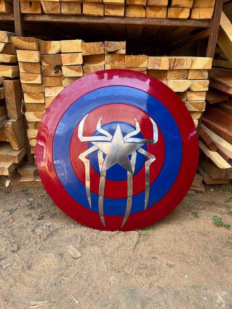 Puede incluir: Un escudo redondo rojo, blanco y azul con una estrella plateada y un dise&ntilde;o de ara&ntilde;a. El escudo es redondo y tiene un borde elevado.