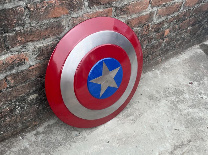 May include: A red, white, and blue Captain America shield with a silver star in the center. The shield is made of metal and has a glossy finish.