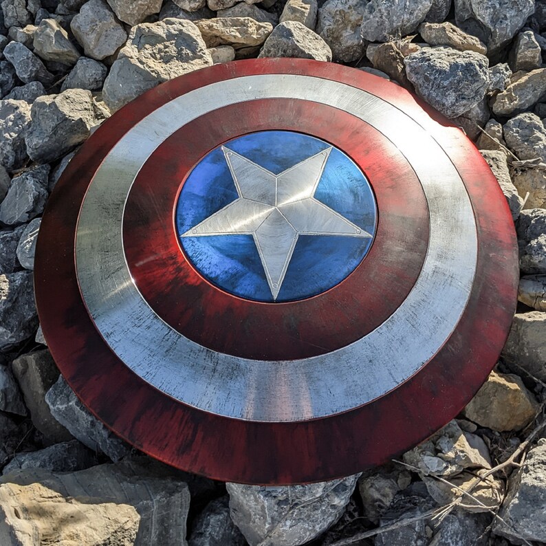 May include: A red, white, and blue Captain America shield with a silver star in the center. The shield has a distressed, weathered look.