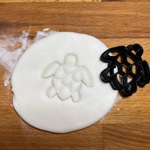 May include: A black plastic turtle cookie cutter with a white fondant imprint of the turtle.