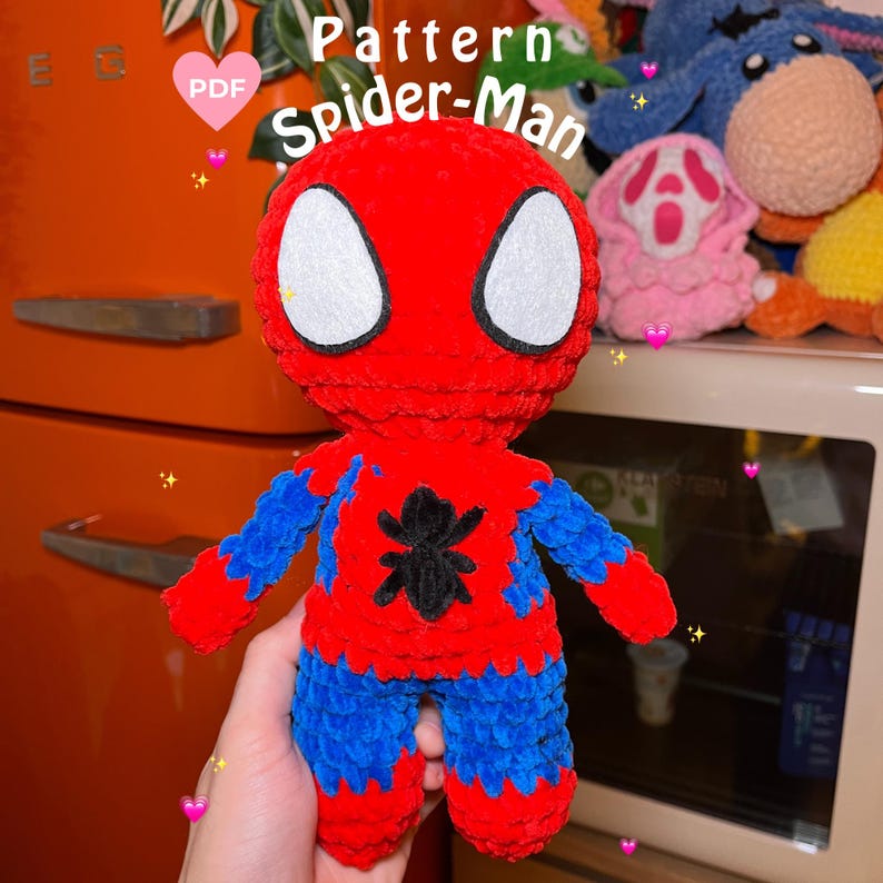 May include: A crocheted amigurumi toy of Spider-Man. The toy is red and blue with a black spider symbol on the chest. The toy has white eyes and a red and blue patterned suit.