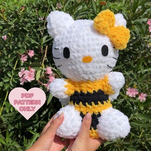Peut inclure: Un jouet en peluche blanc crocheté en forme d'abeille avec un nœud jaune. Le jouet porte une chemise rayée noire et jaune.