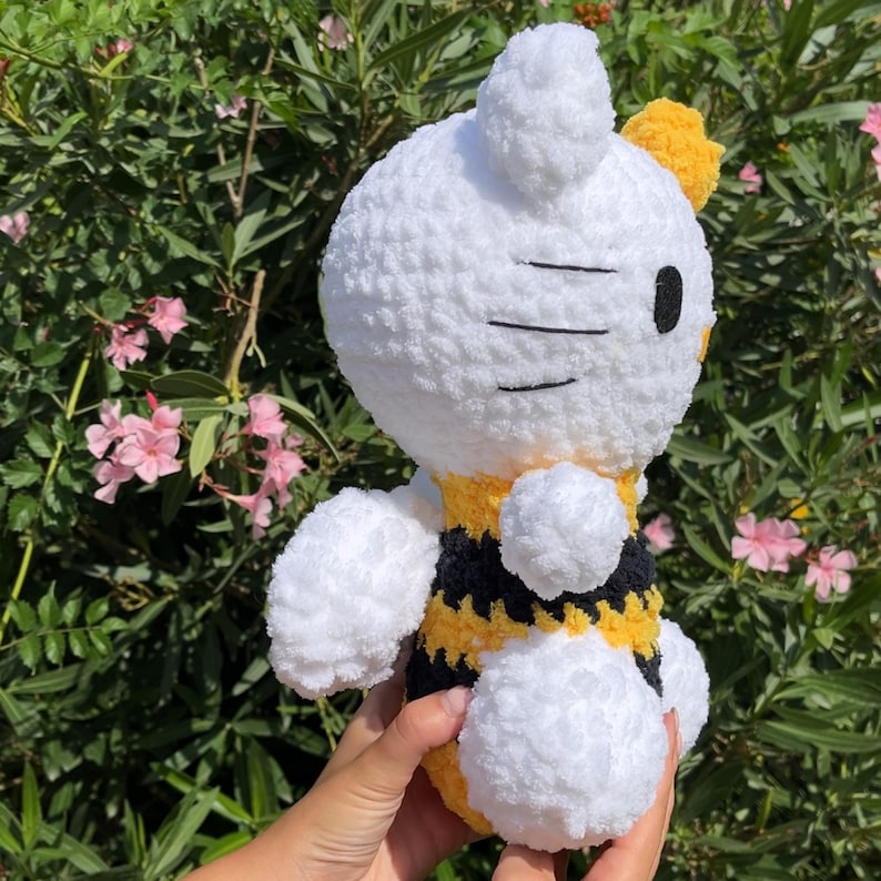 Puede incluir: Juguete de peluche de abeja blanca de crochet con rayas negras y amarillas. La abeja tiene un cuerpo blanco peludo y un ojo negro.