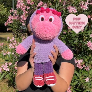 Può includere: Una bambola di peluche fatta a mano nei toni del rosa, viola e rosso. La bambola ha una testa grande con grandi occhi e un cappuccio. Il corpo è viola con accenti rosa sulle mani e sui piedi. I piedi sono rossi con strisce bianche. Il testo "PDF PATTERN ONLY" è su un cuore.