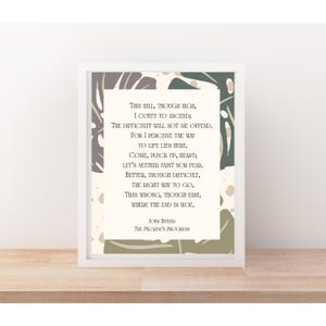May include: A framed print featuring a quote from John Bunyan's "The Pilgrim's Progress." The text is centered on a cream-colored background, surrounded by a white frame. Decorative green and gray leaf-like patterns are in the background.