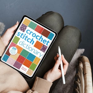May include: A digital tablet displaying a crochet stitch dictionary with 200 essential stitches and step-by-step photos. The title of the book is "crochet stitch dictionary".