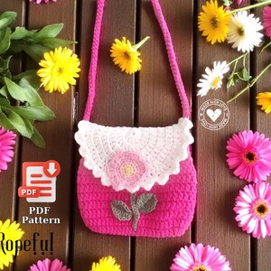 May include: A handmade pink crochet purse with a white scalloped flap and a flower applique. The purse has a pink strap and a floral design. The image also includes the text "PDF Pattern" and "Ropeful".