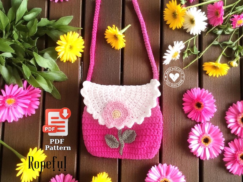 May include: A handmade pink crochet purse with a white scalloped flap and a flower applique. The purse has a pink strap and a floral design. The image also includes the text "PDF Pattern" and "Ropeful".