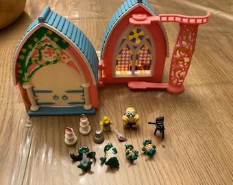 May include: A pink and blue toy church with a decorative balcony, and several small figurines, including frogs in wedding attire, a bird, and a small chair. The church has a stained glass window.