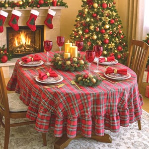 Puede incluir: Una mesa de comedor redonda cubierta con un mantel de cuadros rojos, verdes y blancos con un borde con volantes. La mesa está puesta con platos blancos, servilletas de tela roja en anillos dorados, cubiertos dorados y copas rojas.