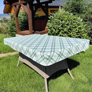 May include: A green and white checkered tablecloth on a wicker table. The tablecloth is made of a durable material and is perfect for outdoor dining.