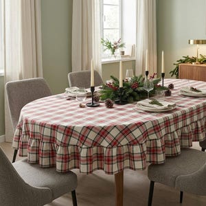 Puede incluir: Un mantel ovalado con un patrón de cuadros rojos, verdes y blancos y un borde con volantes. La tela cubre una mesa de comedor ovalada, dispuesta con platos blancos, vasos transparentes y candelabros negros con velas altas.