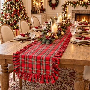 Pode incluir: Um caminho de mesa xadrez vermelho e verde com bordas franzidas sobre uma mesa de jantar de madeira. O caminho apresenta um padr&atilde;o tartan cl&aacute;ssico com linhas finas amarelas e pretas. &Eacute; decorado com casti&ccedil;ais de vidro e ramos de pinheiro.