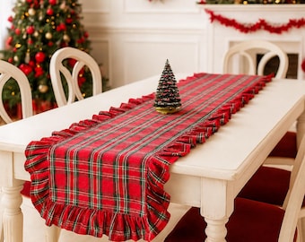 Pode incluir: Um caminho de mesa retangular com um padrão xadrez em vermelho, verde e branco, com bordas franzidas nas laterais. O caminho de tecido está estendido sobre uma mesa de jantar branca, com uma pequena árvore de Natal artificial decorativa.