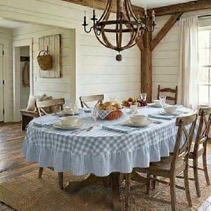 May include: A dining room featuring a wooden table covered with a light blue and white checkered tablecloth with a ruffled edge. The table is set with white bowls, a basket of bread, and a large wooden chandelier hangs above the table.