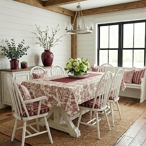 May include: A dining room set featuring a wooden table covered with a red and white toile patterned tablecloth, surrounded by white spindle-back chairs with matching red and white striped cushions, set on a natural fibre area rug.