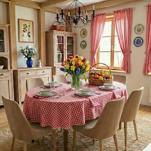May include: An oval dining table covered with a red and white checkered tablecloth, set with white plates and bowls. A large bouquet of colorful flowers and a wicker basket filled with assorted fruits sit in the center. Six chairs surround the table.
