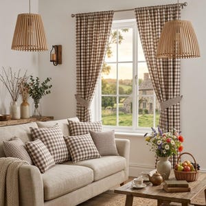 May include: A cozy living room scene featuring a beige sofa with checkered throw pillows. Brown and white checkered curtains frame a window overlooking a rural landscape. Two wooden pendant lights hang from the ceiling, complementing the rustic decor.