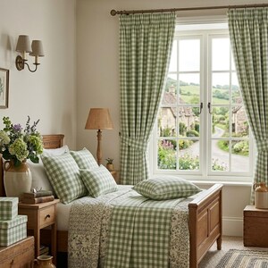 May include: A cozy bedroom scene featuring a wooden bed with green and white checkered bedding and pillows. Matching checkered curtains frame a window overlooking a quaint village. A woven lamp and floral arrangements add to the room's charm.