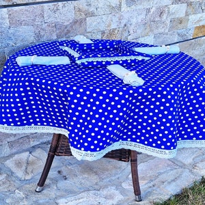 May include: A blue and white polka dot tablecloth with white lace trim. The tablecloth is laid out on a round table with a wicker base.