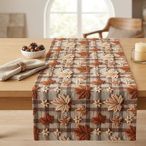 May include: A rectangular table runner featuring a brown and beige plaid pattern decorated with three-dimensional fabric maple leaves in shades of orange, brown, and tan, arranged in a repeating design across the entire surface of the textile.
