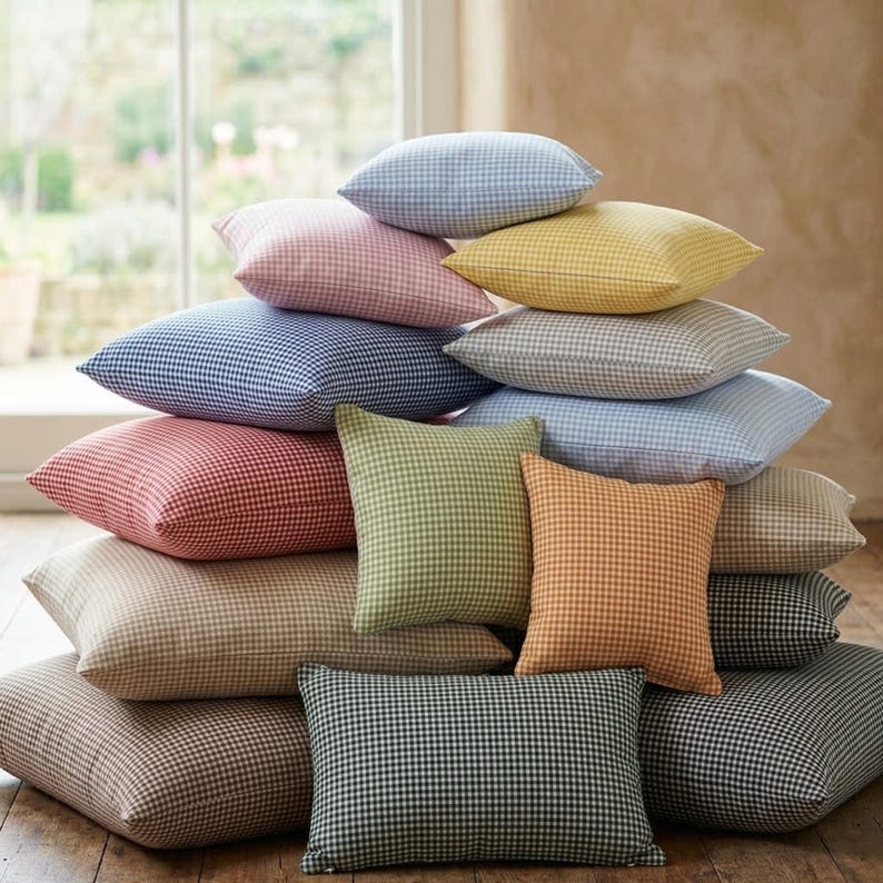 May include: A stack of various-sized pillows in a variety of colors, including blue, pink, yellow, green, and orange. Each pillow features a gingham pattern. The pillows are arranged on a wooden surface.