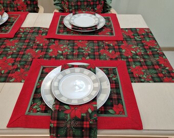 Pode incluir: Um corredor de mesa vermelho e verde xadrez com um design de poinsettia. O corredor de mesa está posto com um prato branco e um prato branco menor em cima. O corredor de mesa está sobre uma mesa de madeira.