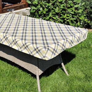 Könnte beinhalten: Eine gelbe und schwarze karierte Tischdecke auf einem Tisch aus Weide. Die Tischdecke ist aus gewebtem Stoff und hat einen Fransenrand.