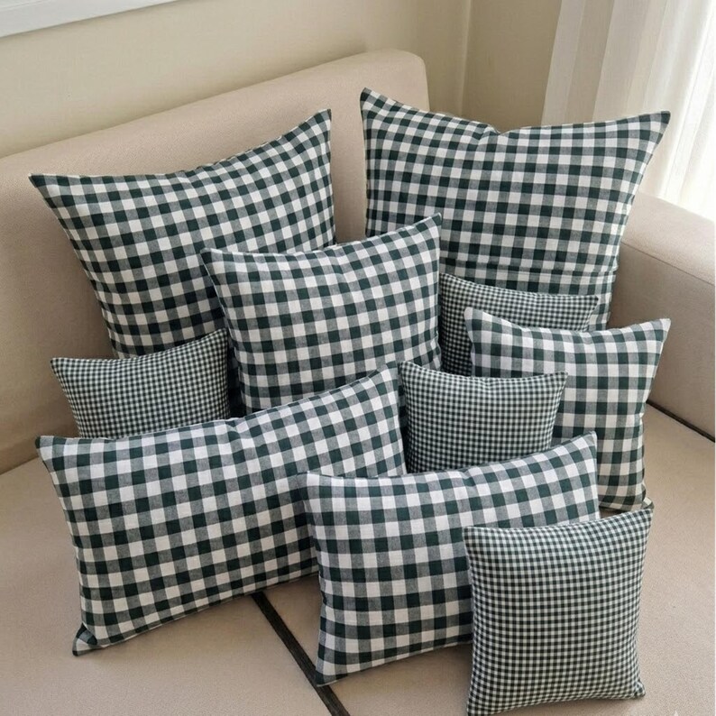 May include: A collection of green and white checkered throw pillows of various sizes arranged on a beige sofa. The pillows have a classic gingham pattern, creating a cozy and inviting aesthetic. The arrangement includes square and rectangular shapes.