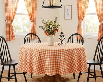 May include: A round dining table covered with an orange and white gingham tablecloth, surrounded by four black spindle-back chairs. A white vase filled with wildflowers and a black metal candle holder sit on the table surface.