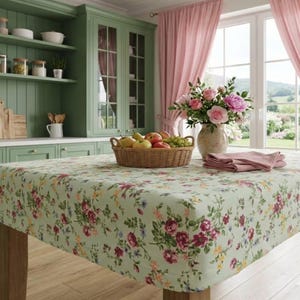 Peut inclure: Une nappe à motifs floraux vert clair recouvre une table en bois. Le motif comprend des roses rouges et roses et d'autres fleurs. Un panier de fruits et un vase de fleurs sont sur la table. La cuisine a des armoires vertes.