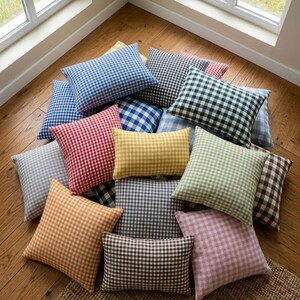 May include: A collection of square and rectangular throw pillows in various colors, including blue, red, green, yellow, and brown. Each pillow features a classic gingham check pattern. The pillows are arranged on a wooden floor.