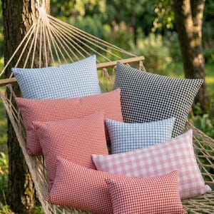 May include: A collection of gingham-patterned pillows in various colors, including red, blue, pink, and black, arranged on a hammock. The pillows have a classic checkered design, perfect for outdoor decor.