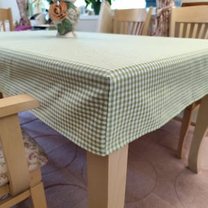 Könnte beinhalten: Eine hellgrüne und weiß karierte Tischdecke bedeckt einen Holztisch. Die rechteckige Tischdecke hat ein klassisches Vichy-Muster. Der Tisch steht in einem Esszimmer mit Holzstühlen.