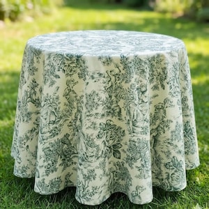 May include: A round tablecloth featuring a cream-coloured fabric with a repeating dark green toile pattern. The design depicts various figures, floral arrangements, and landscape elements distributed across the entire surface of the textile.
