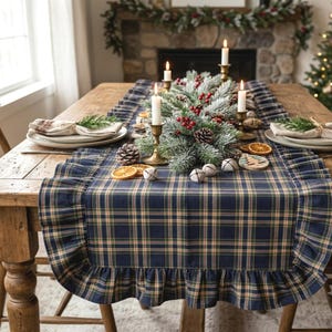 Pode incluir: Um caminho de mesa xadrez azul-marinho, verde e bege com bordas franzidas. O caminho &eacute; decorado com um centro de mesa de ramos de pinheiro geados, bagas vermelhas, pinhas, guizos brancos, fatias de laranja secas e casti&ccedil;ais de lat&atilde;o.