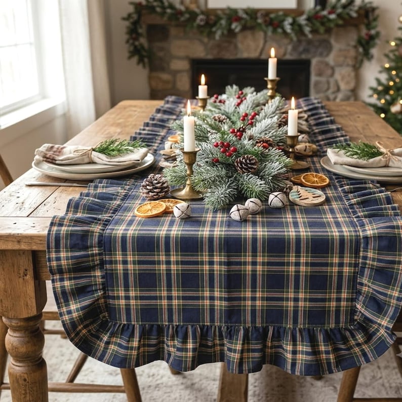 Pode incluir: Um caminho de mesa xadrez azul-marinho, verde e bege com bordas franzidas. O caminho &eacute; decorado com um centro de mesa de ramos de pinheiro geados, bagas vermelhas, pinhas, guizos brancos, fatias de laranja secas e casti&ccedil;ais de lat&atilde;o.