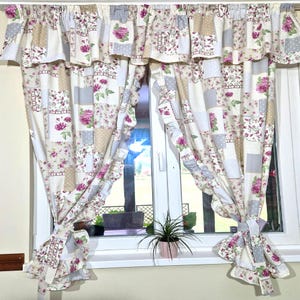 Könnte beinhalten: Ein Paar weiße und beige Patchwork-Vorhänge mit rosa floralen Akzenten und gekräuselten Rändern. Die Vorhänge sind mit einer Schleife zurückgebunden und hängen an einem Fenster.