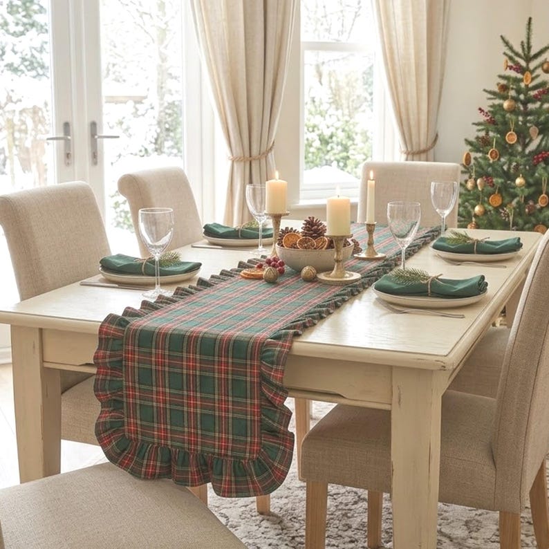 Pode incluir: Um caminho de mesa retangular com padr&atilde;o xadrez verde, vermelho e branco e bordas com babados. O caminho est&aacute; colocado sobre uma mesa de jantar de madeira clara, posta com pratos brancos, guardanapos verde-escuros e velas.